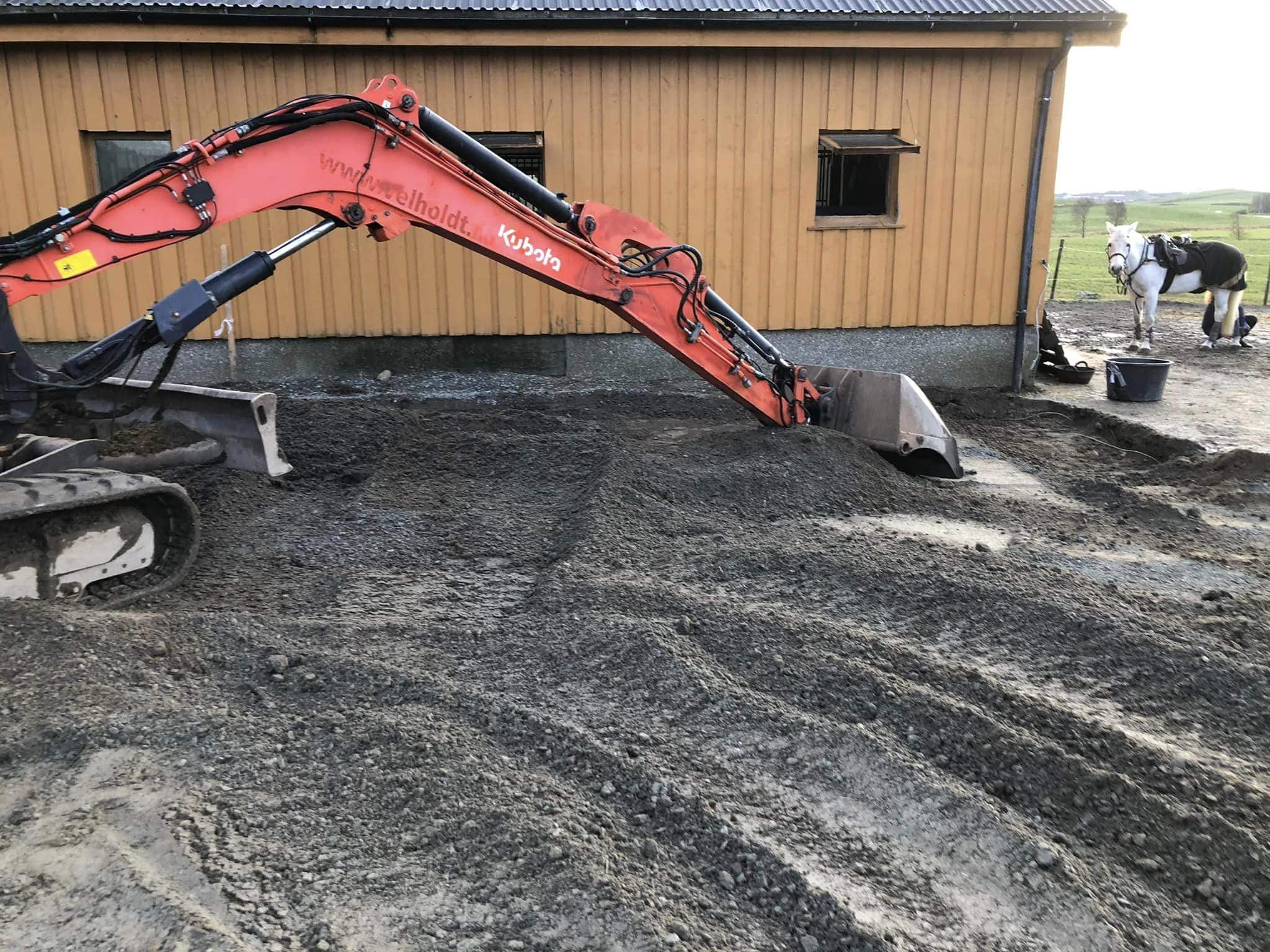 Excavator working near wooden barn.